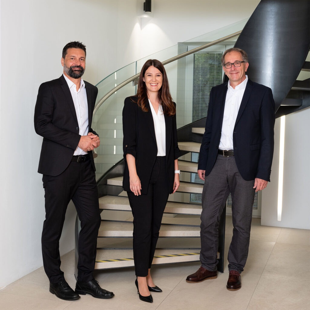Foto von Alexander Zlotek, Cornelia Springer und Markus Lechleitner - nebeneinander stehend vor modernem Treppenaufgang